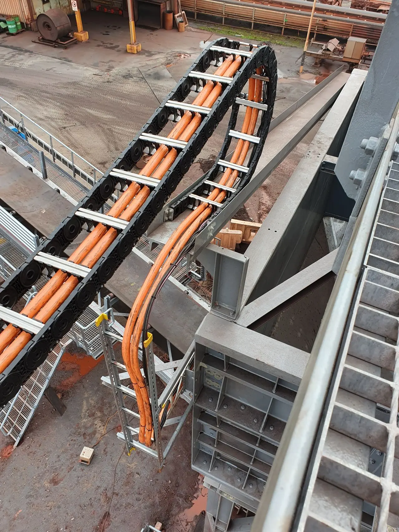 Tsubaki Kabelschlepp kabelrups gemonteerd op een uitschuifbare arm in een stoffige industriële omgeving